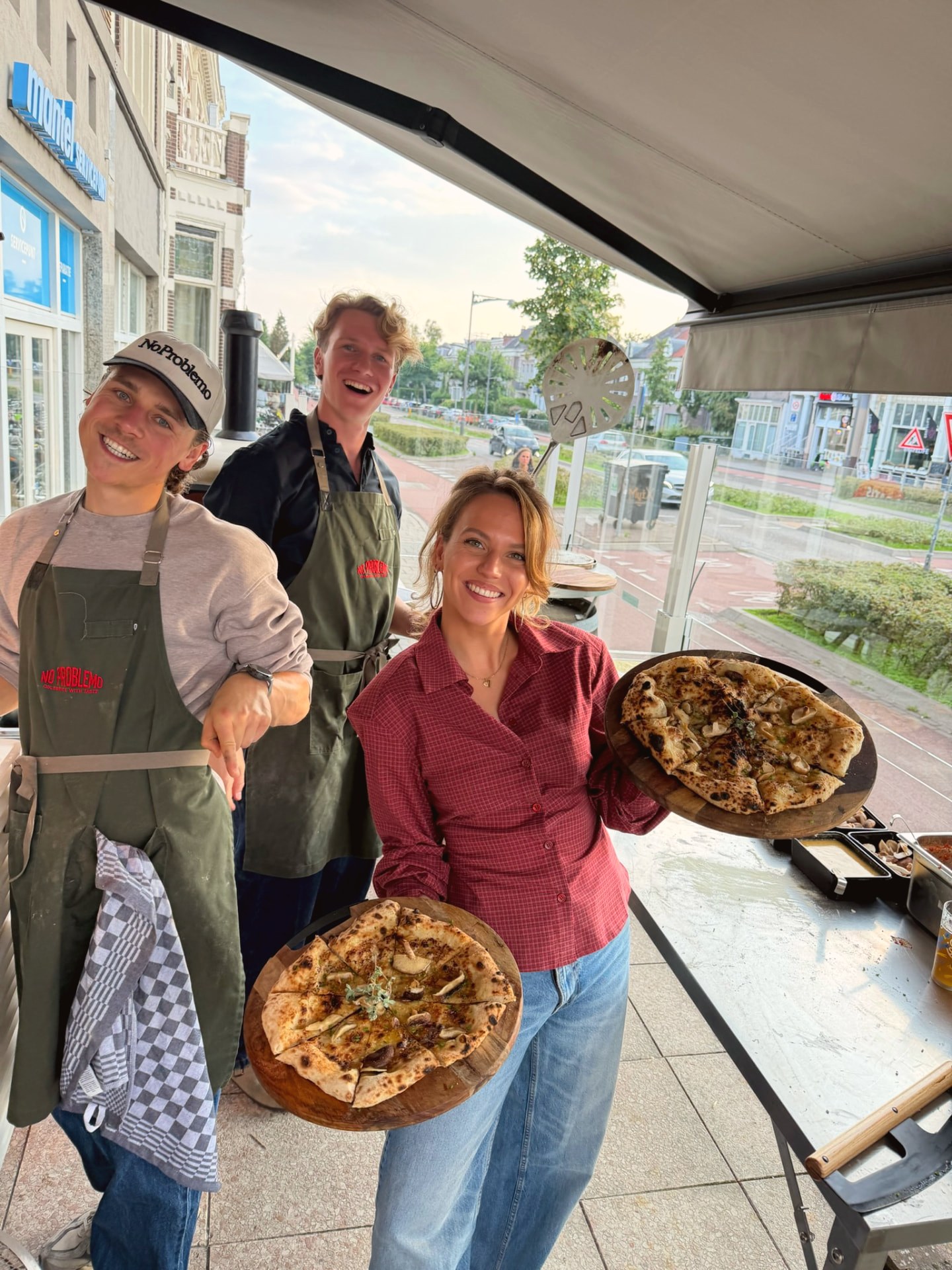 Het team van No Problemo met twee verse pizza's buiten de winkel