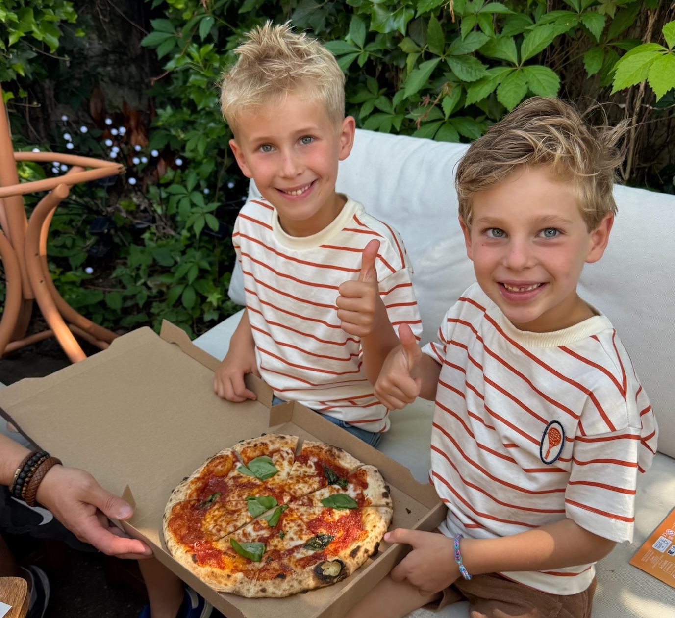 Twee blije jongens met een verse margherita pizza in de tuin